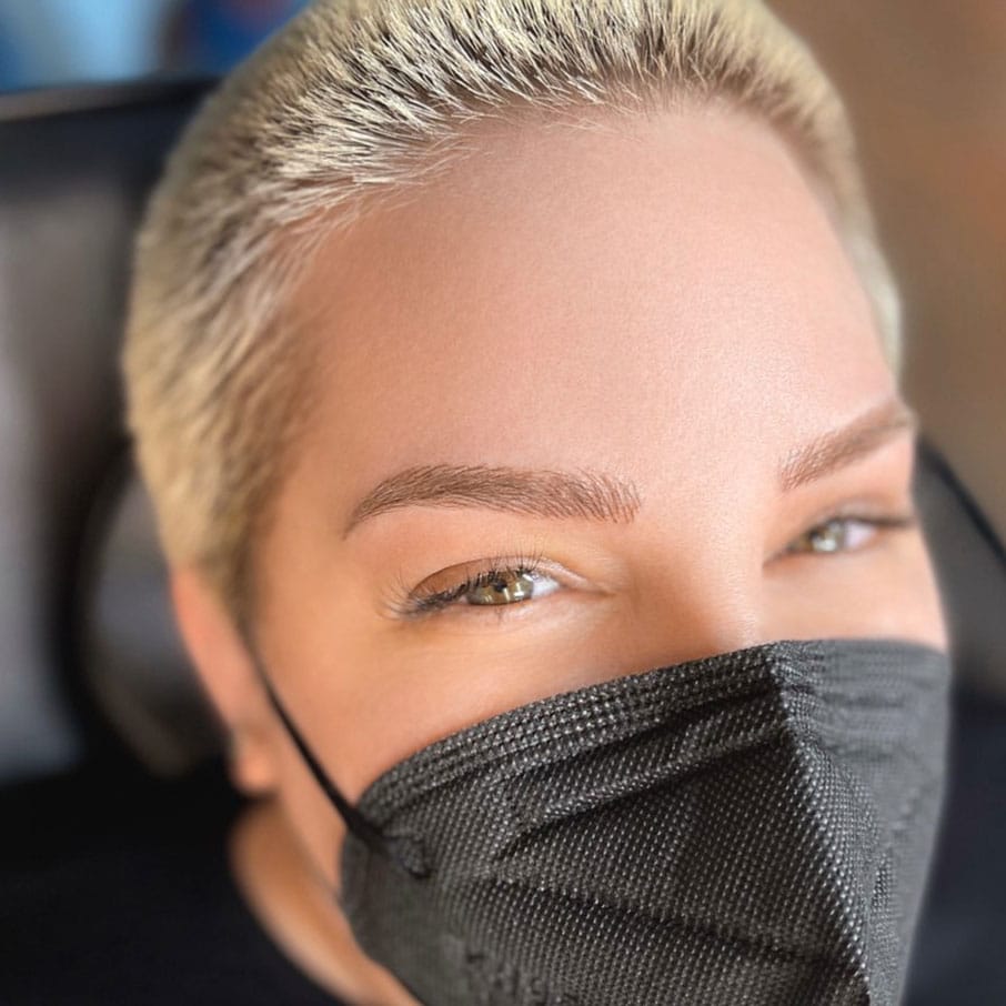 A woman with short blonde hair wearing a black mask.